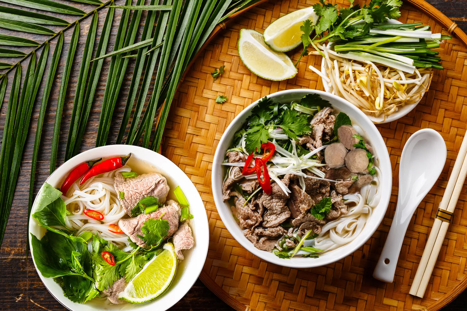 Two bowls of Vietnamese pho with rare beef, herbs, bean sprouts and lime